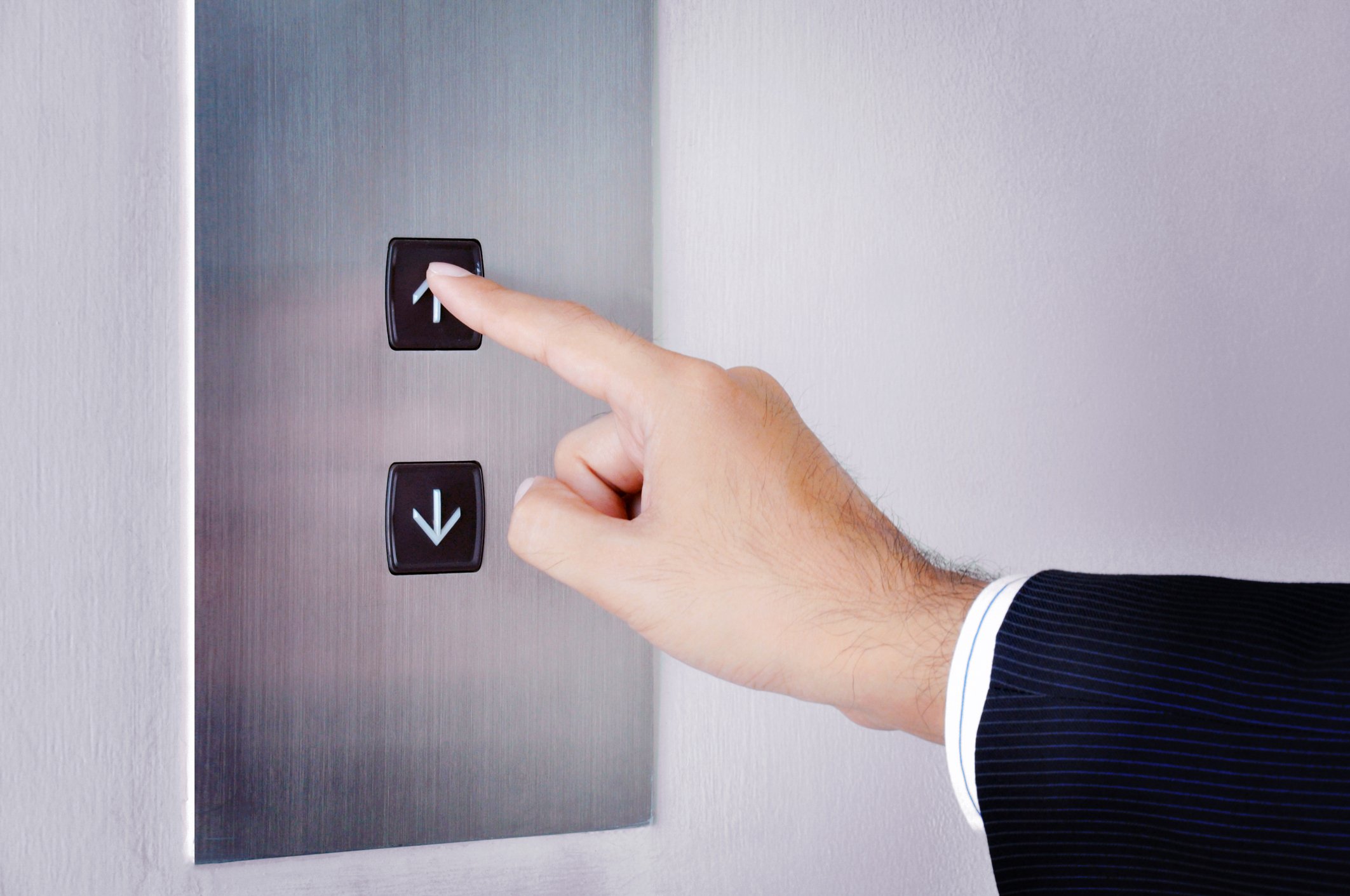 A businessman presses the up button in an elevator.