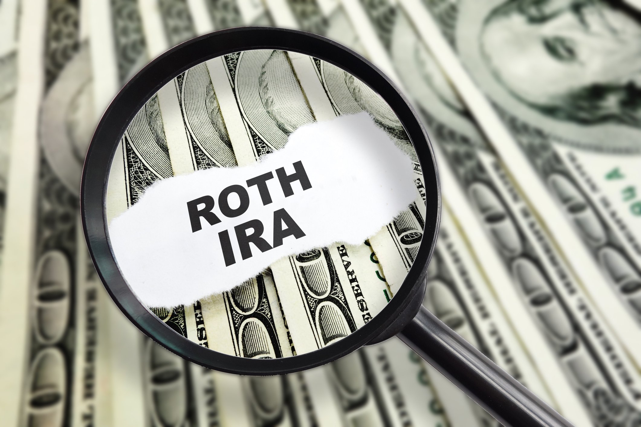 Magnifying glass over the words "Roth IRA" with dollar bills in the background
