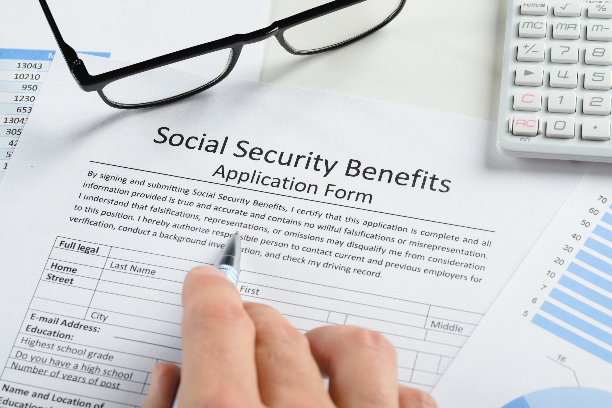 Glasses and a calculator sit next to a Social Security application that a person is filling out.