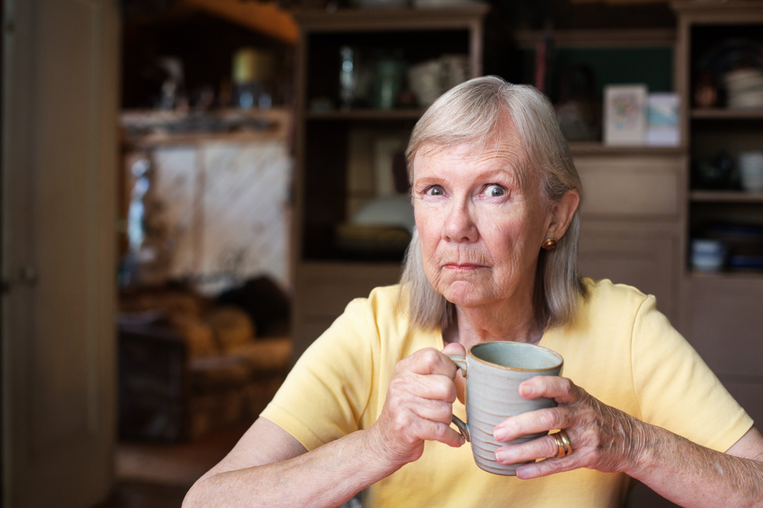 An older woman, clutching a cup in her hands, casts a suspicious look.
