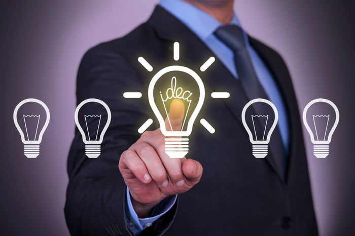 A businessman points at a lit up light bulb in a row of light bulbs.
