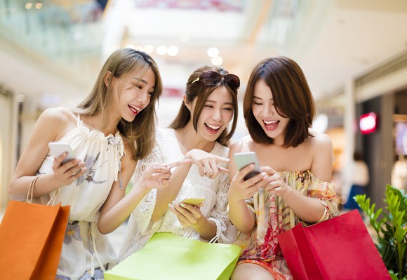 Three young Chinese women laughing, using their smartphones. 