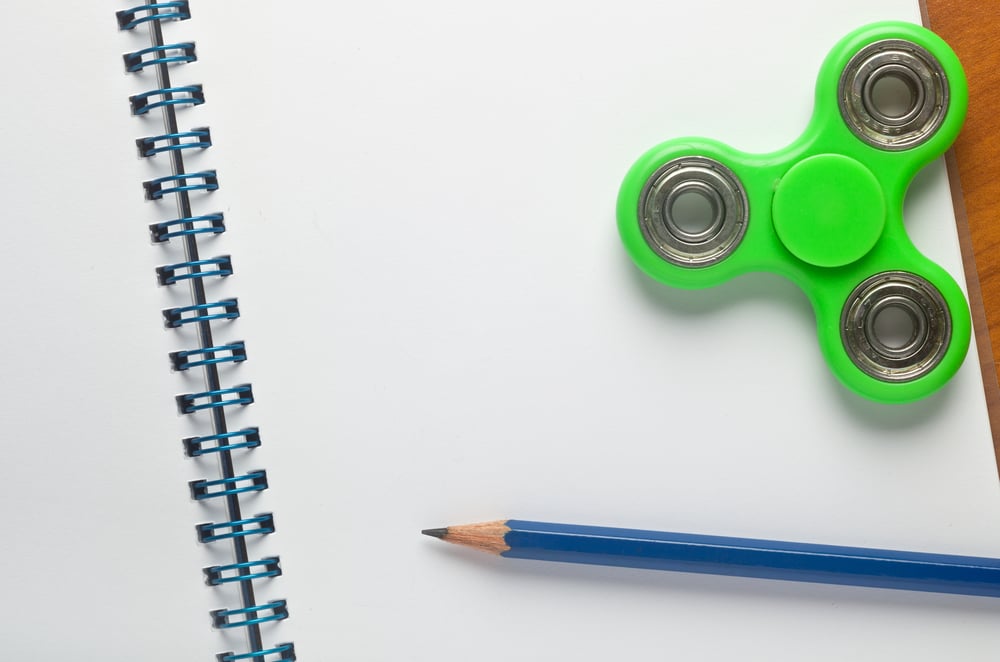 Green fidget spinner toy on notebook with blue pencil.