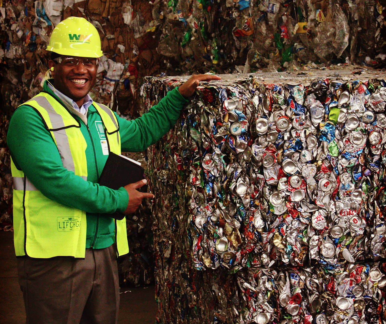 Waste Management employee standing near a large amount of recycled materials and smiling