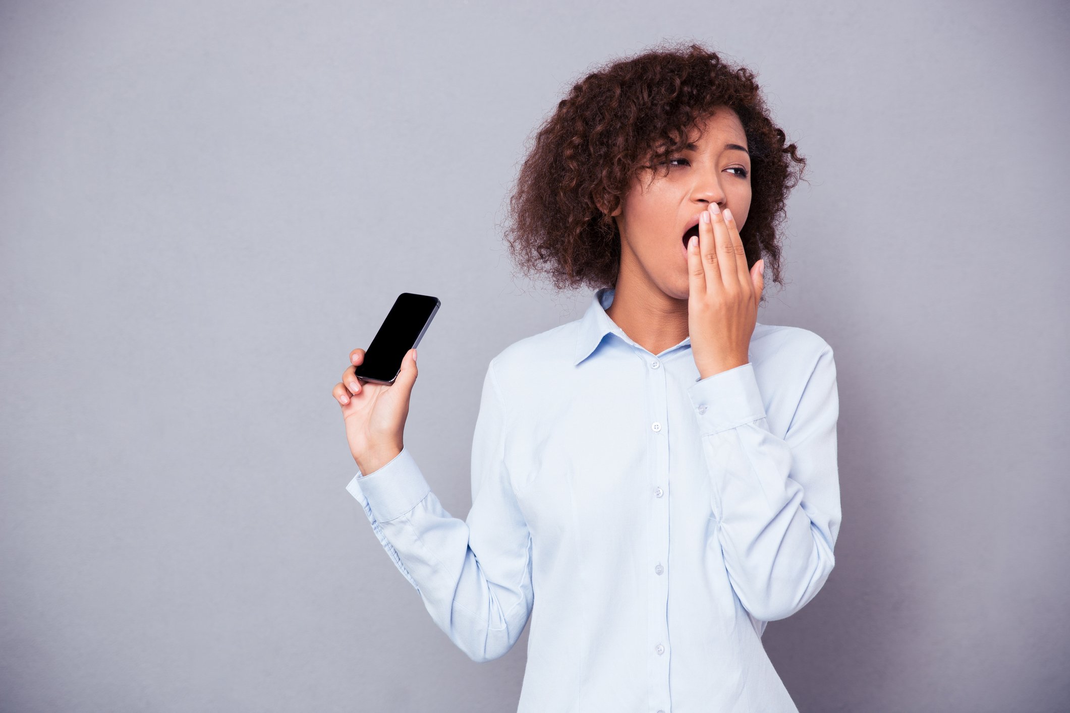 Woman holding a smartphone while yawning.