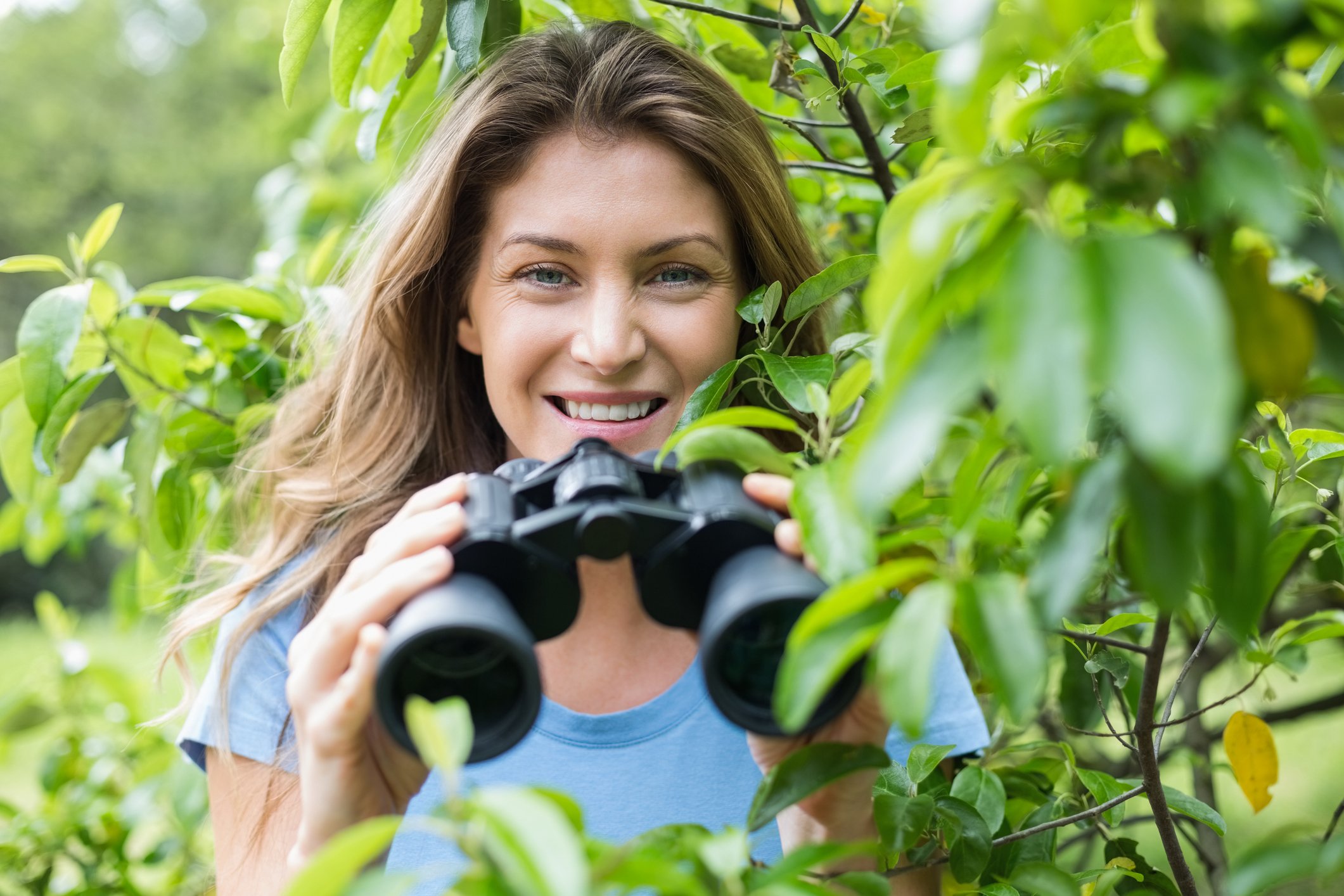 Woman behind some bushes, with binoculars and a big smile.