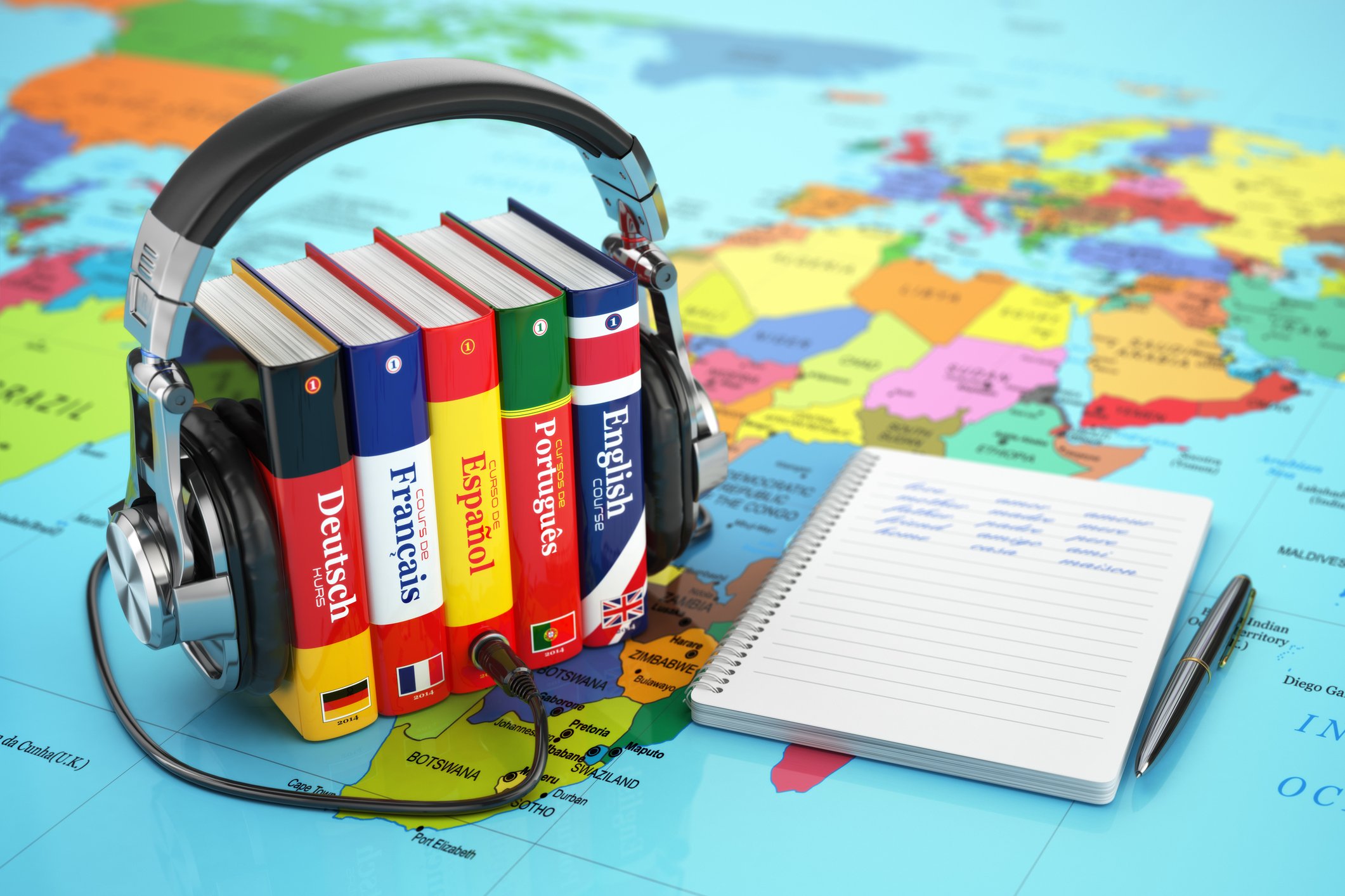 A pair of headphones are wrapped around a group of foreign-language dictionaries, sitting on a map and lying next to a pen and pad of paper.