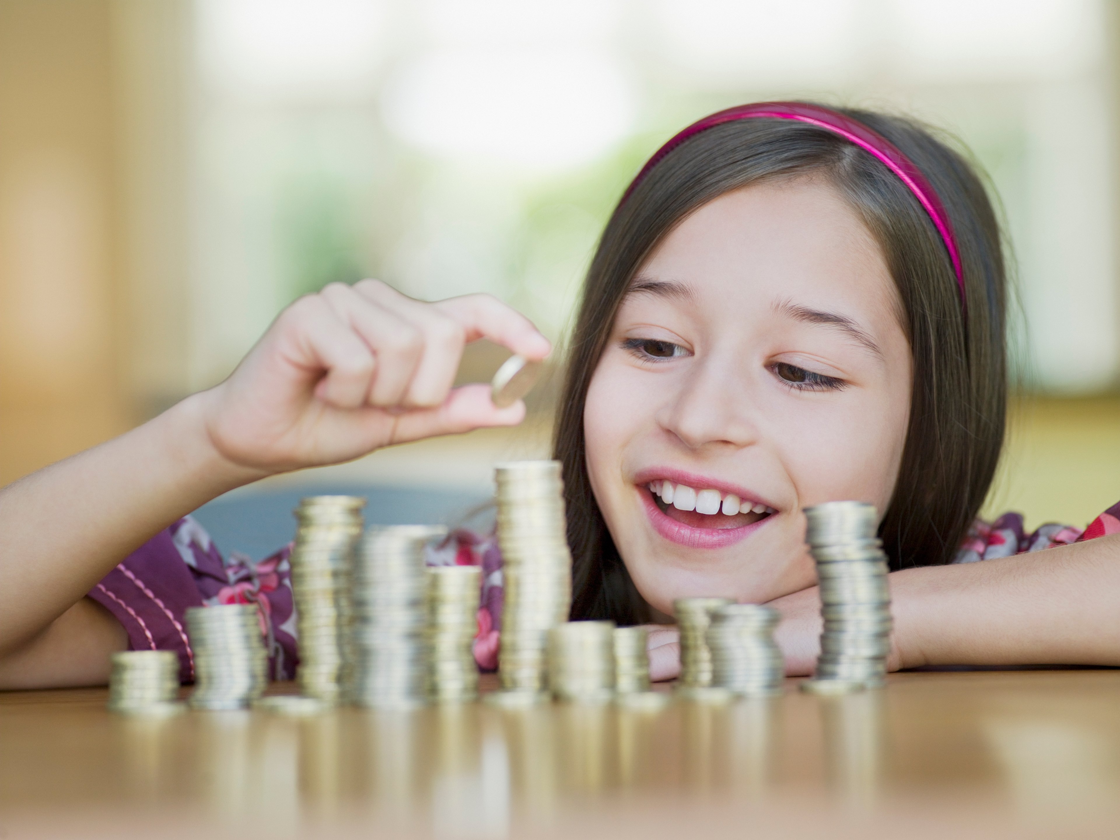A smiling young girl prepares to place a coin on one of several stacks in front of her.