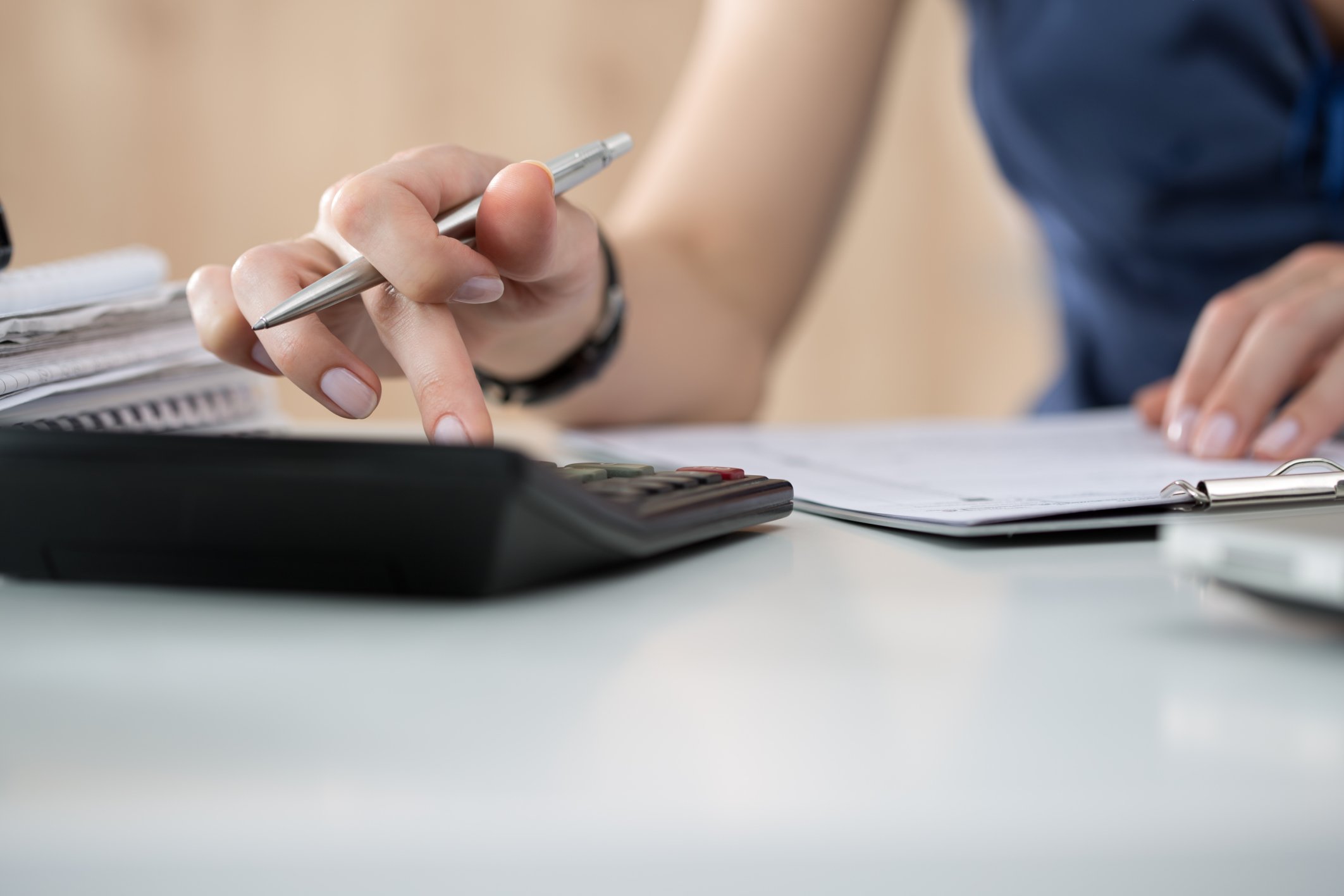 A woman with a pen in her hand uses a calculator.