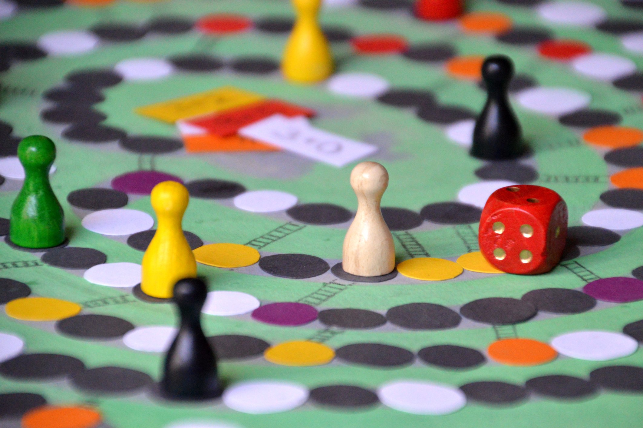 Several colorful pawns and a red die are positioned on a game board.