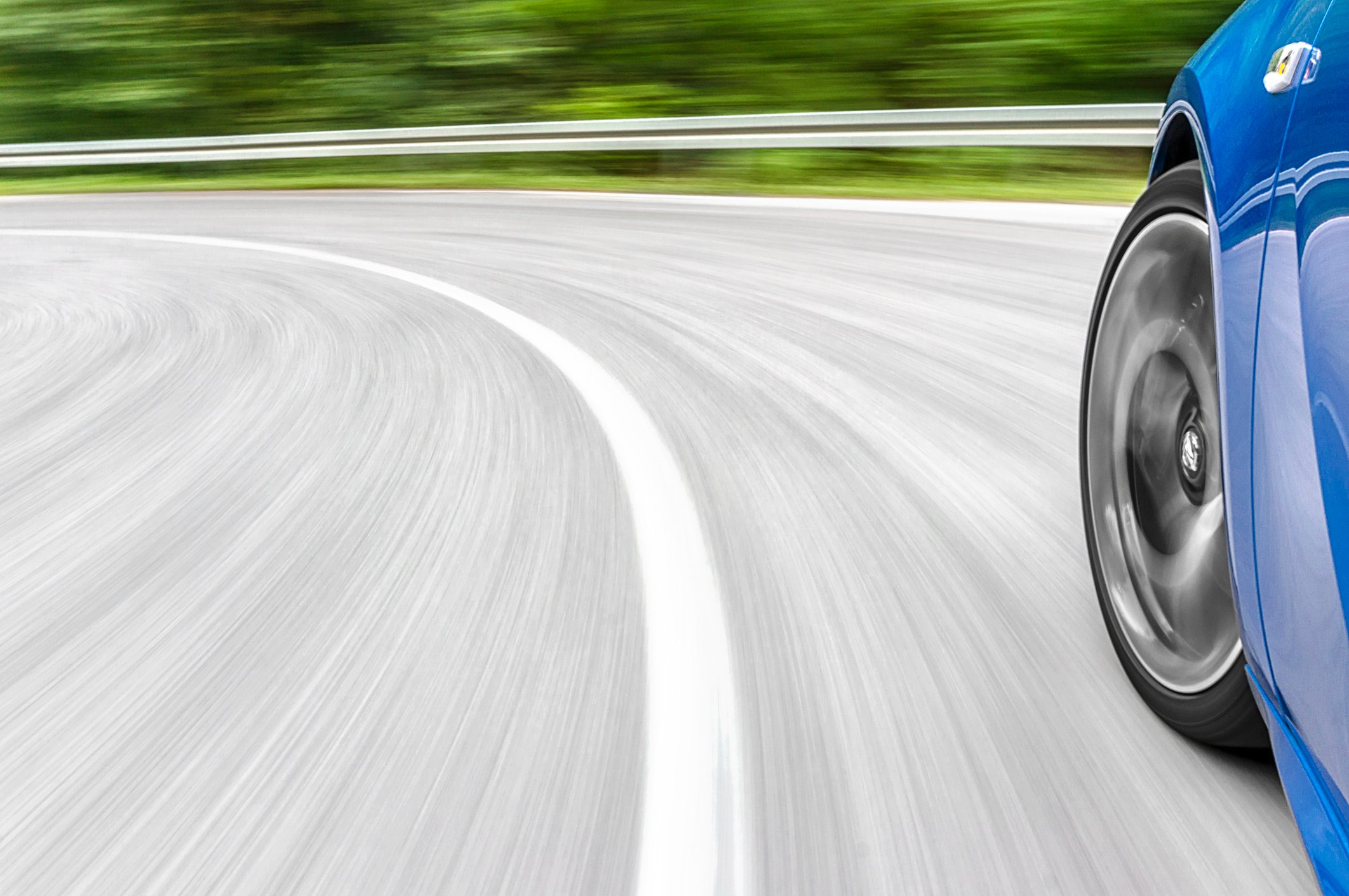 Motion blur shot of  a car driving fast on the road, showing the front corner of the car from a side view.