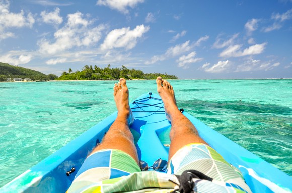 Man wearing board shorts sitting on the ocean with islands in the background.
