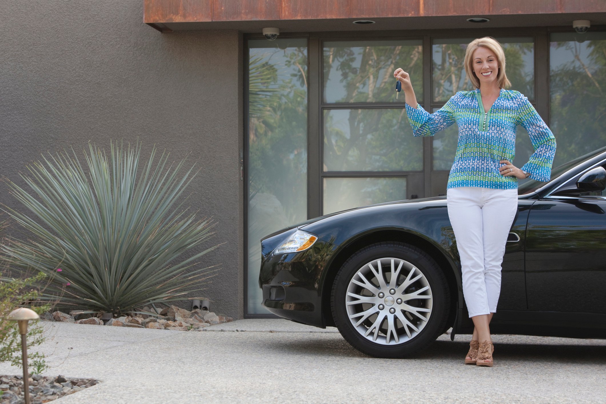 A smiling woman holds up a set of car keys as she stands next to a parked car.
