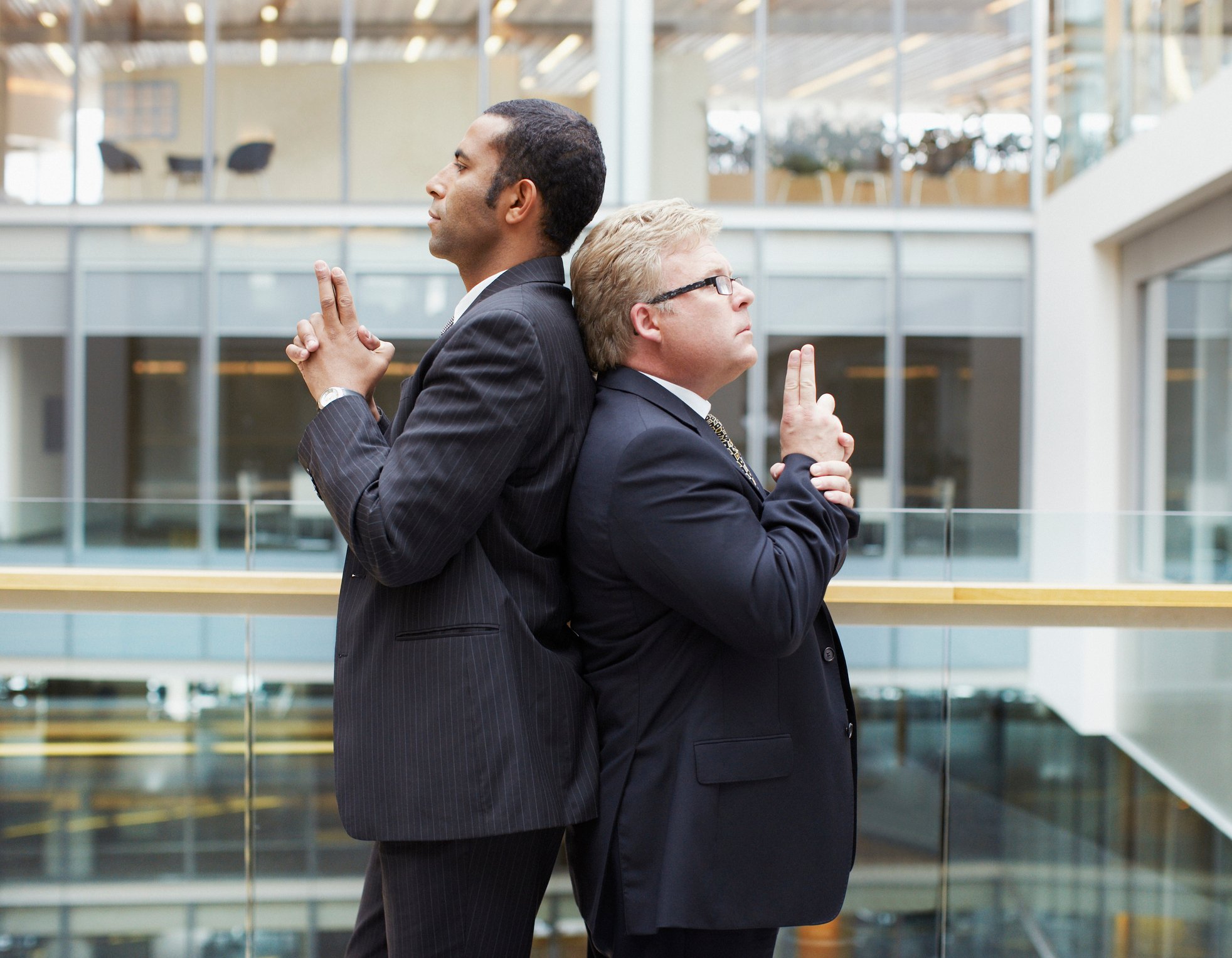 Businessmen back to back fighting symbolic duel with fingers raised as weapons.
