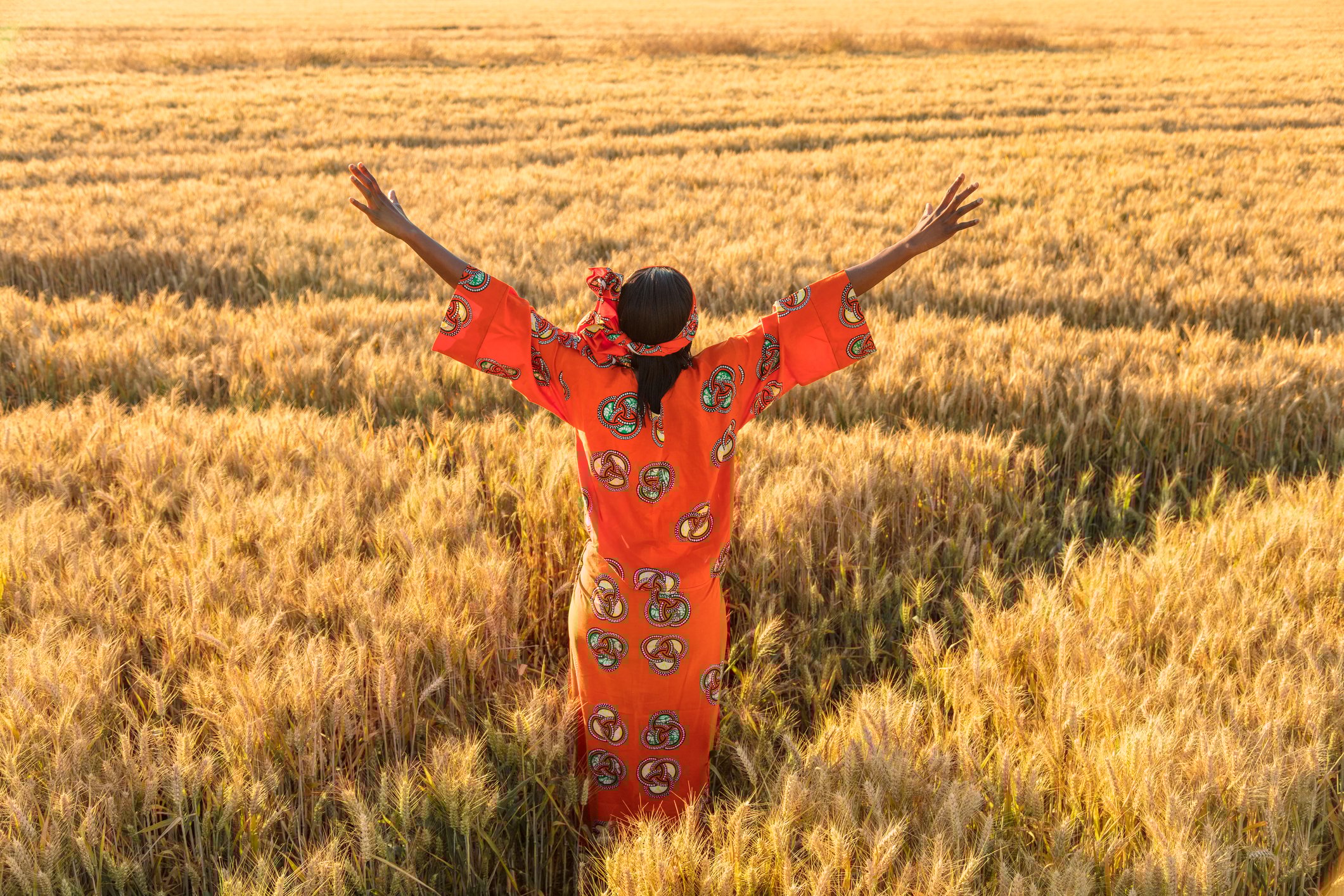 An indigenous woman with arms raised triumphantly toward an open field.