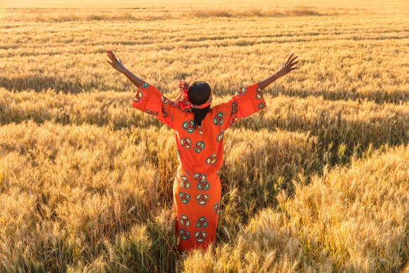 An indigenous woman with arms raised triumphantly toward an open field.