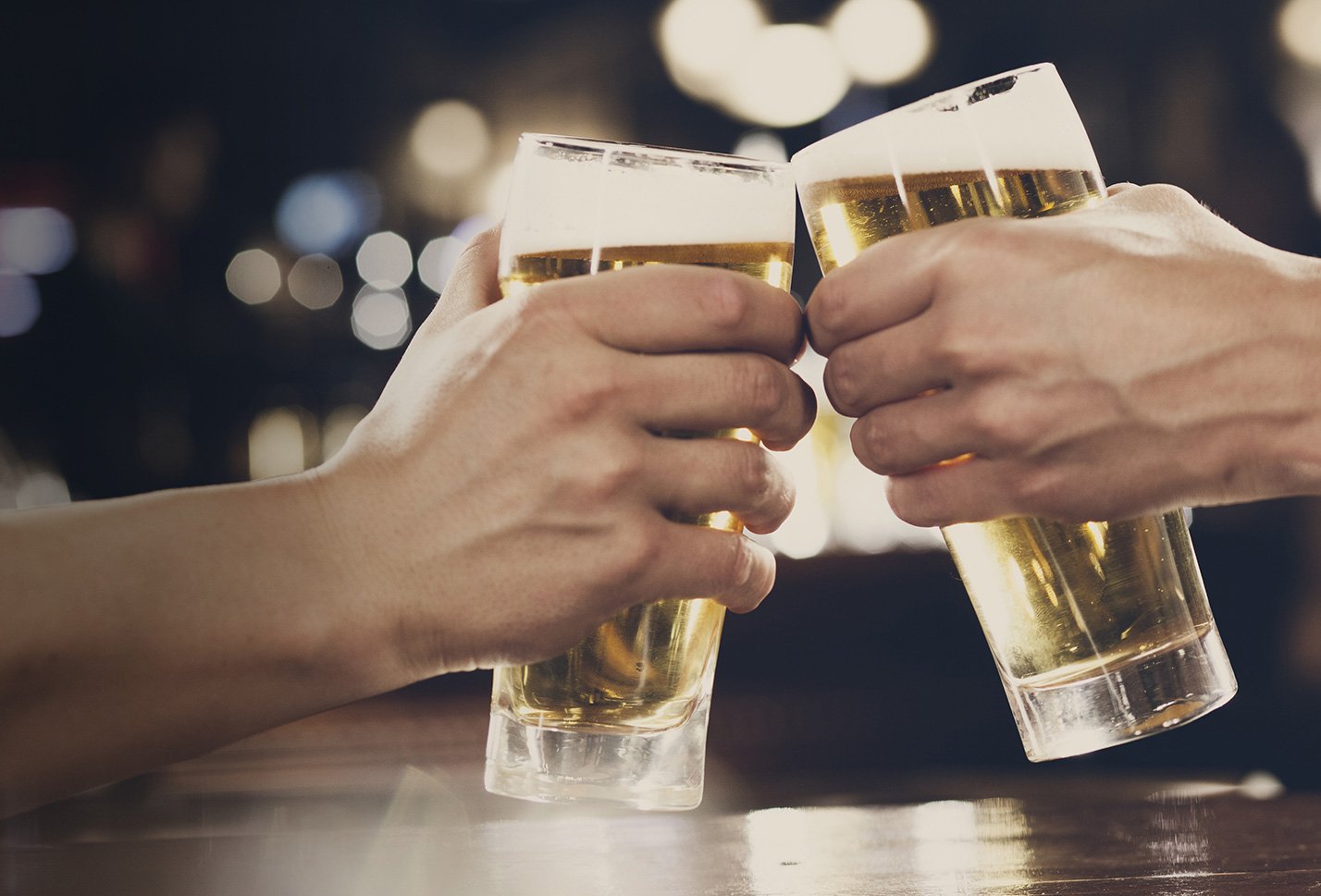 Two hands clink beer glasses together in a toast.