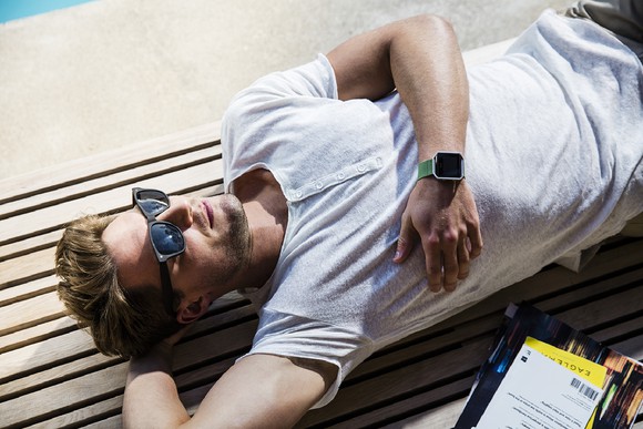 Man in t-shirt and sunglasses lying down relaxing with Fitbit on his wrist.