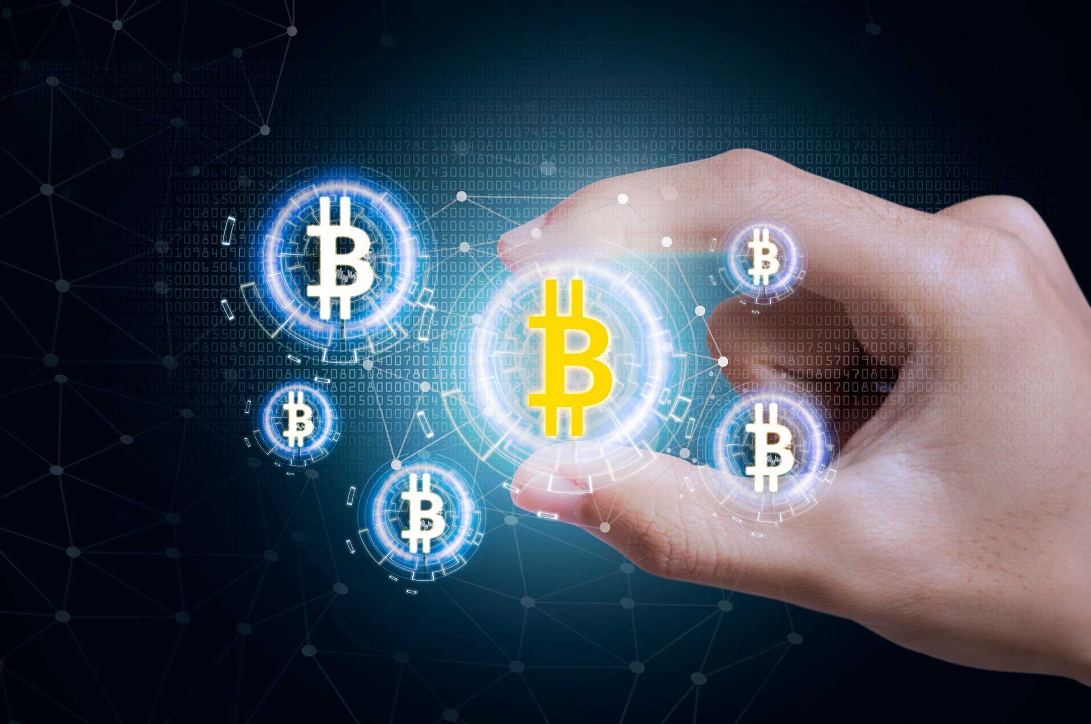 Conceptual image of a hand holding a digital depiction of a bitcoin with other digital depictions of coins surrounding it.