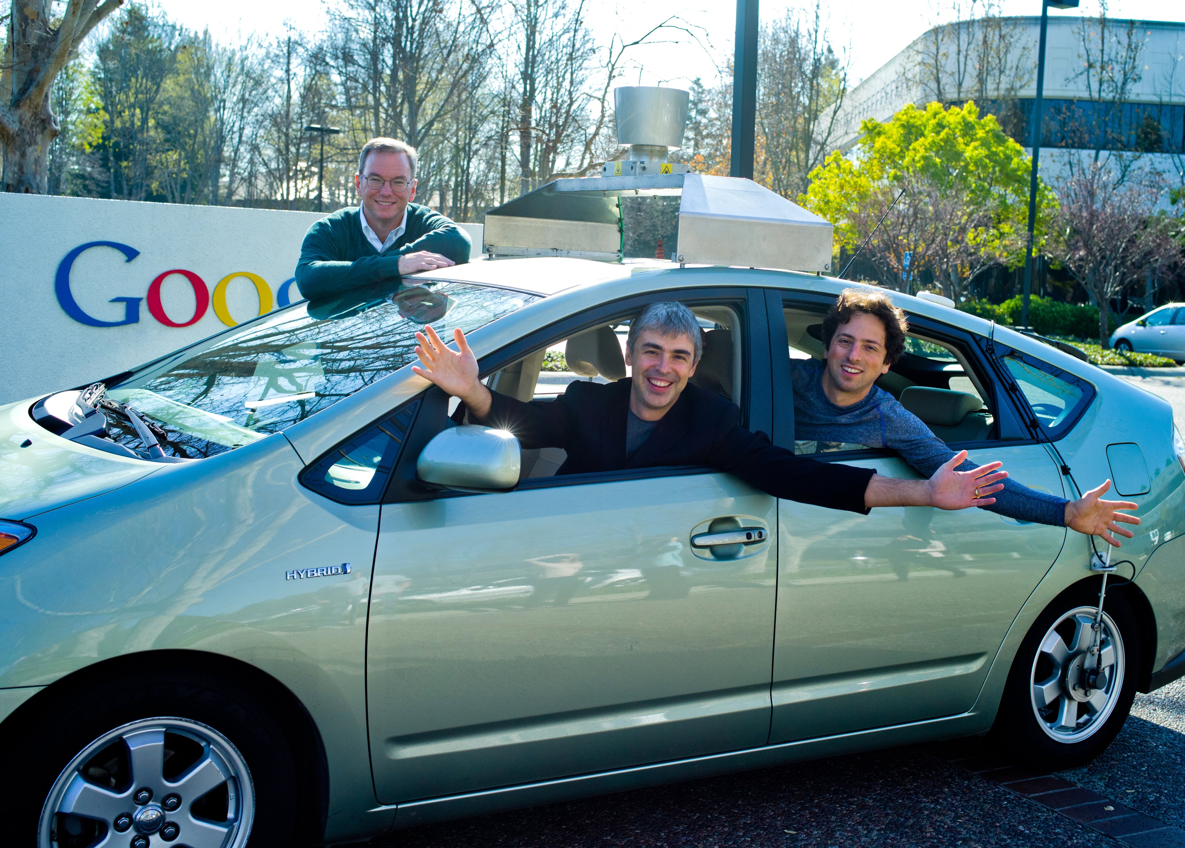 The three men are leaning out the windows of a modified Prius, parked in a Google parking lot. 