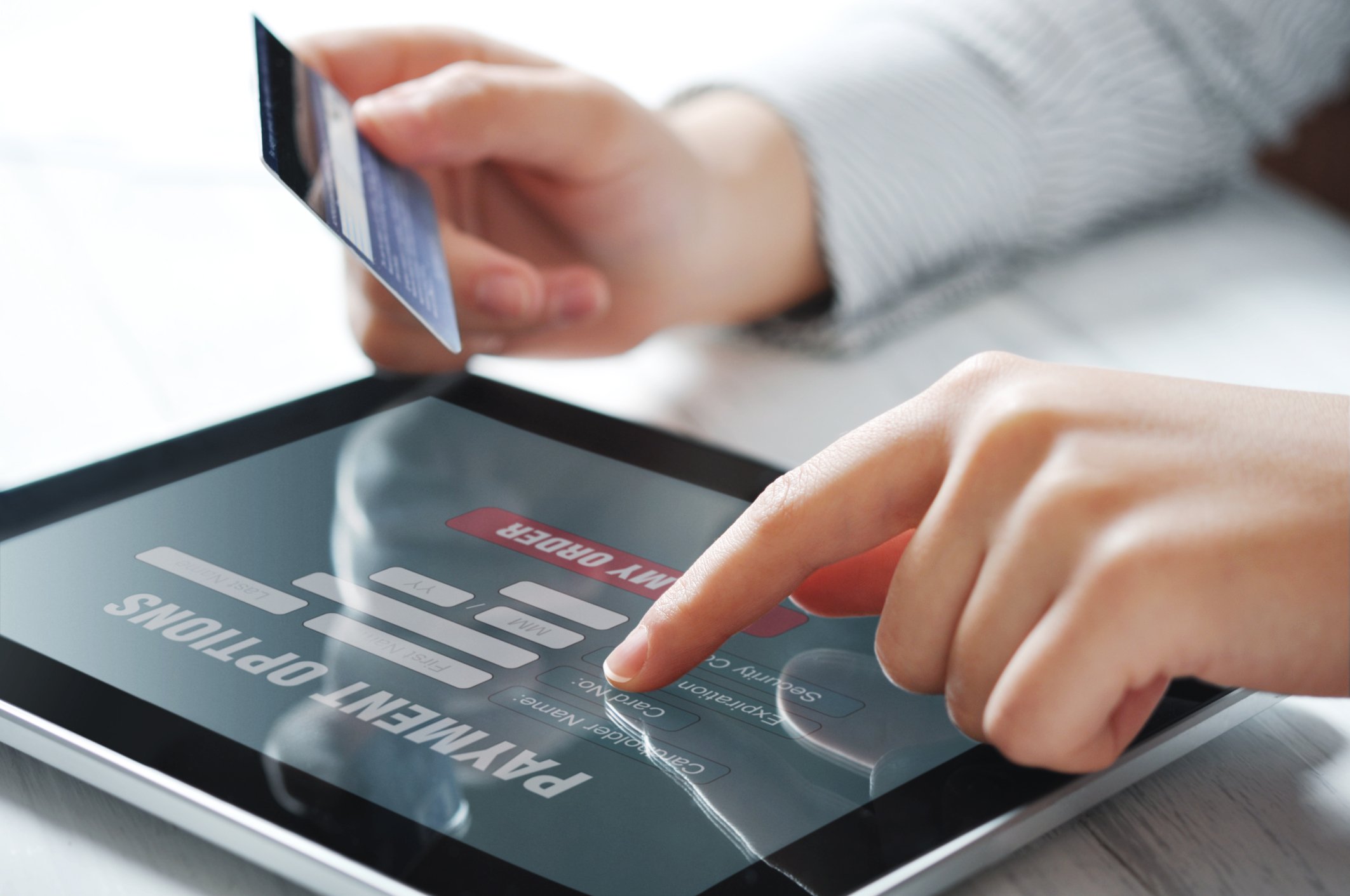 A person holds a credit card while shopping on a tablet.