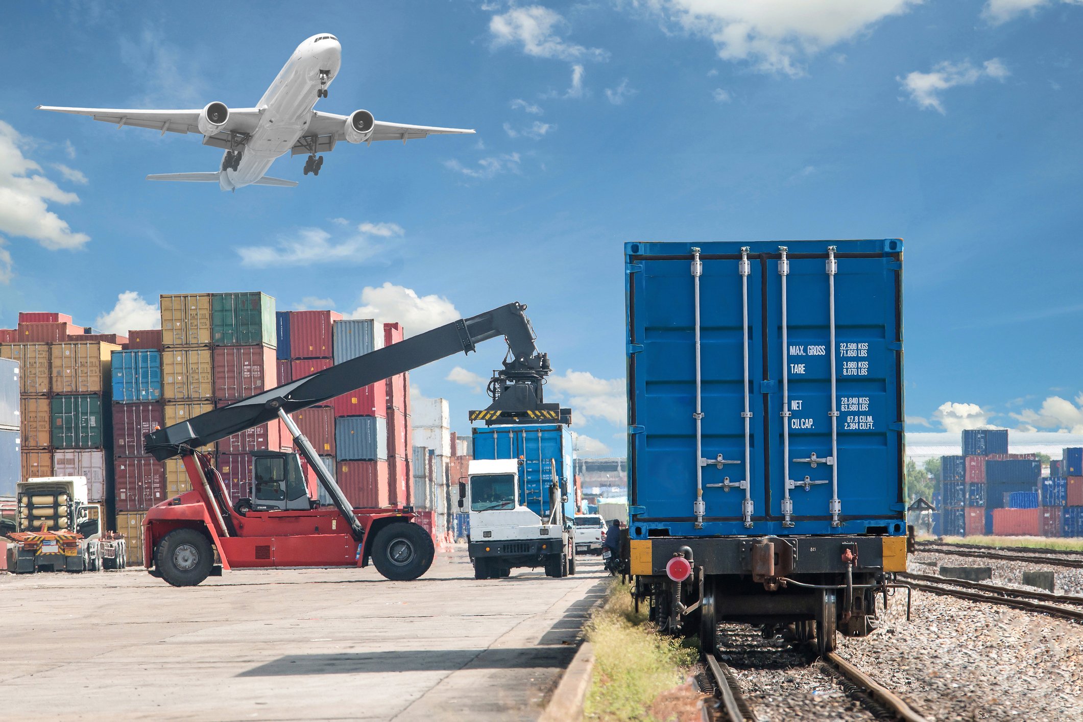 Freight being loaded onto trucks while an airplane flies overhead.