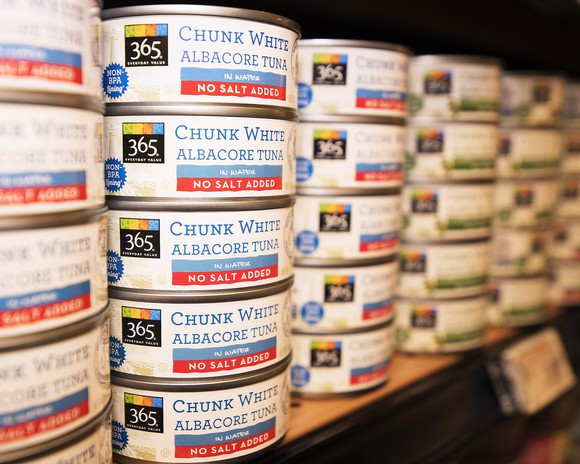 Cans of Whole Foods 365 tuna, stacked on a store shelf.