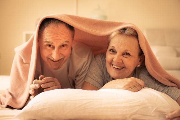 An elderly couple peeking out from underneath their sheets.