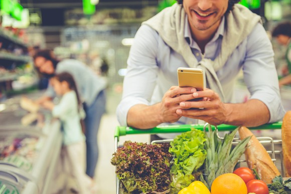 A man checking his phone while shopping for groceries.