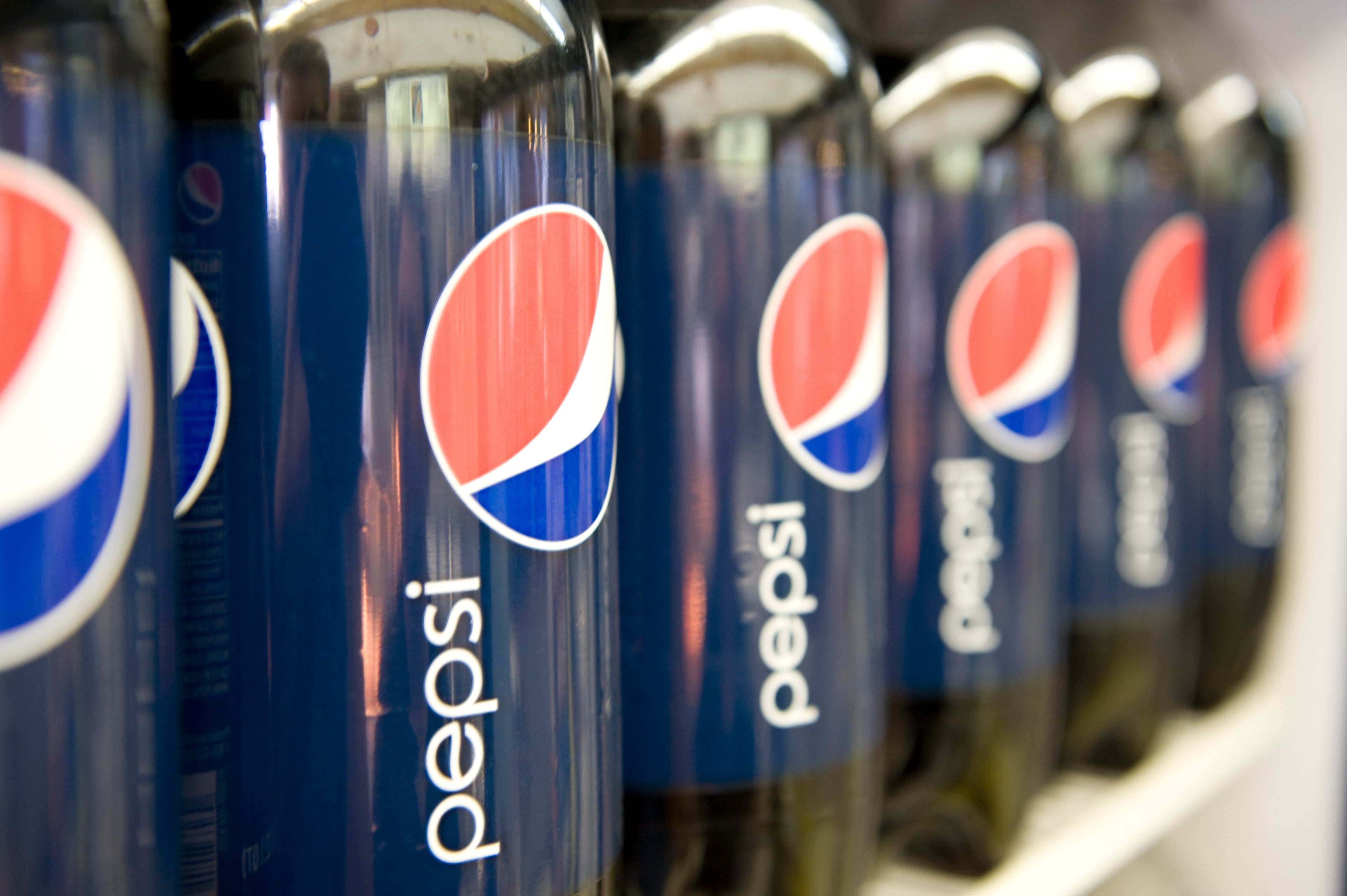 Plastic bottles of Pepsi are lined up on a shelf.
