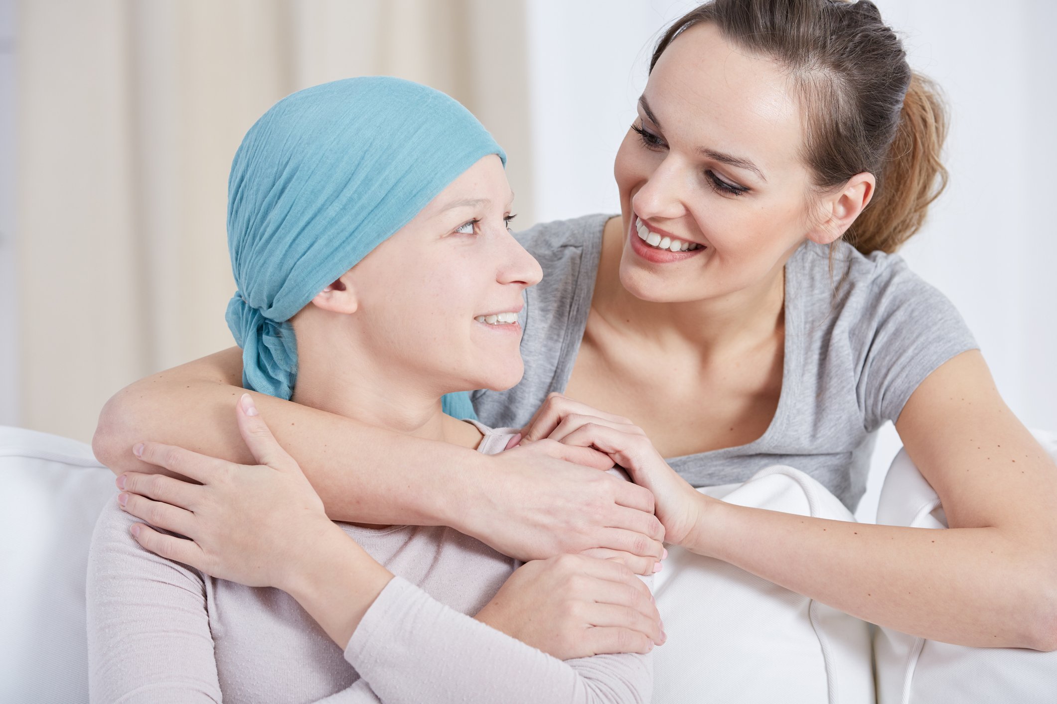 Two smiling women embracing; one is wearing a scarf to cover hair loss