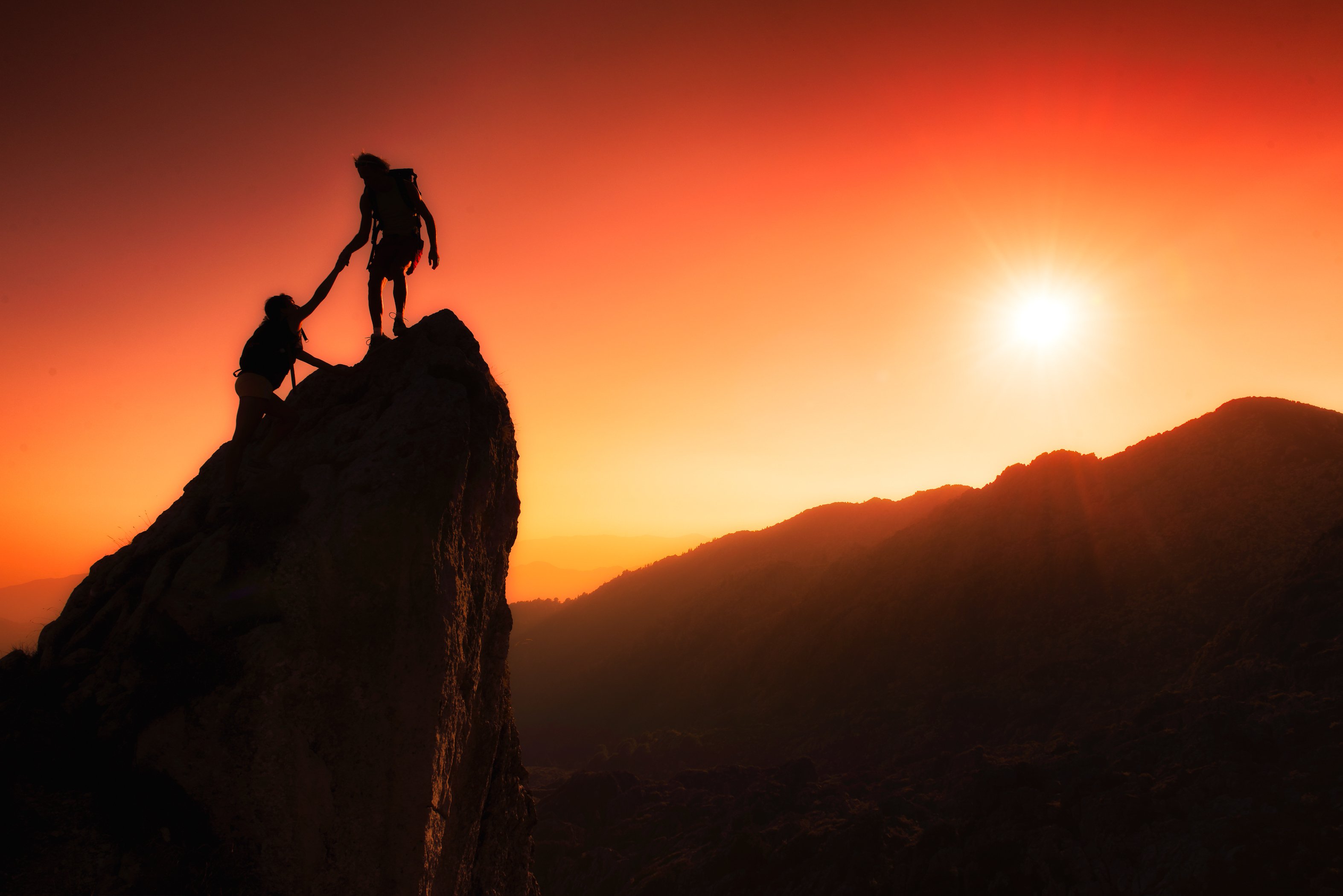 Two mountain climbers reaching the summit at sunset.