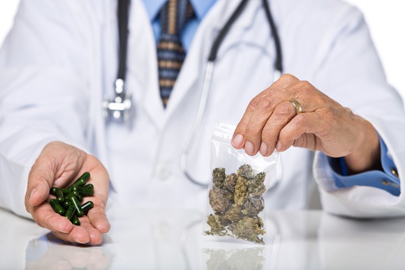 A doctor holding cannabis buds in one hand and cannabis-infused pills in the other.