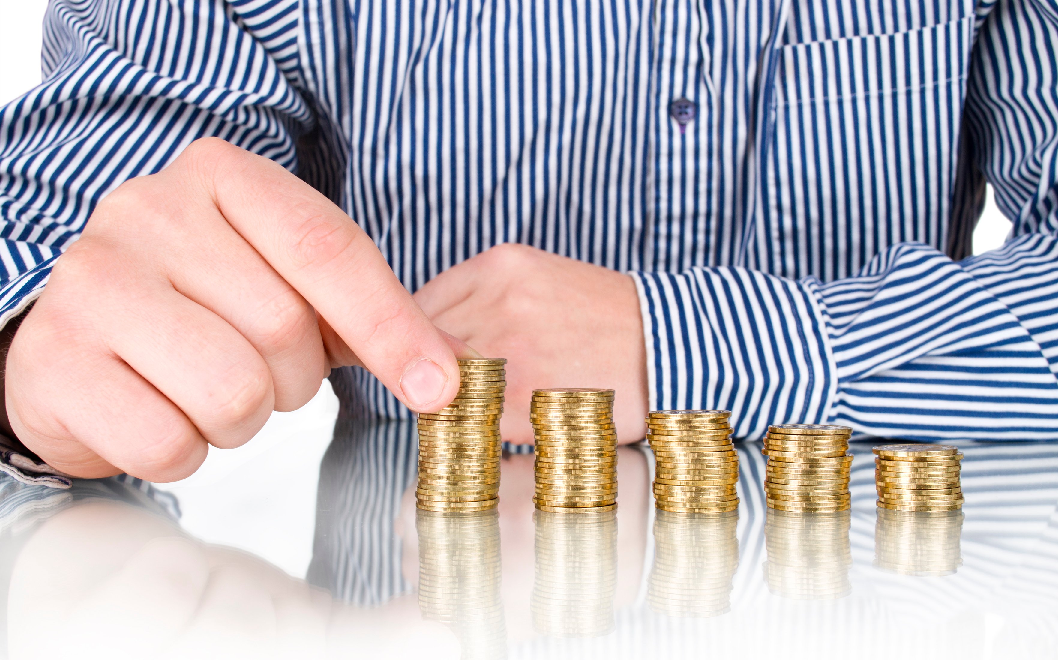 Sitting behind a stack of progressively taller stacks of coins, a man prepares to place a coin on the highest stack.