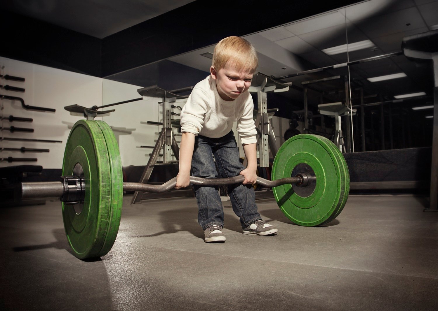 A small child tries to lift a very heavy barbell.