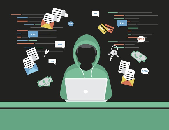 A hooded figure sits in front of a laptop.