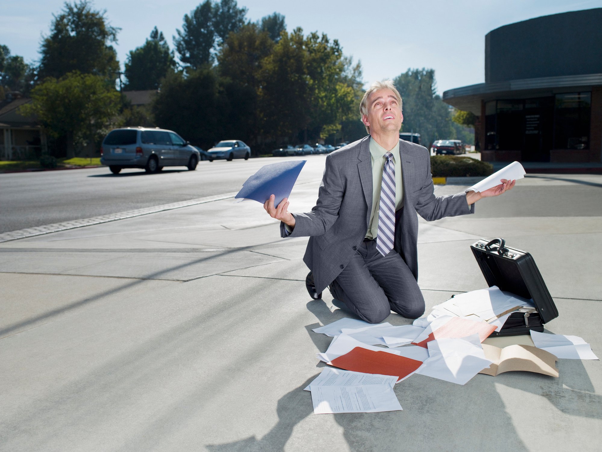 Frustrated businessman kneeling over a heap of unsorted papers.