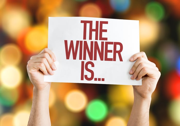 Woman's hands holding up a sign that says "The Winner Is..."