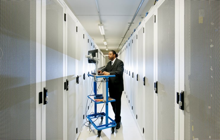 A worker on a computer stands amid rows of servers, like those used by internet giant Google and Facebook