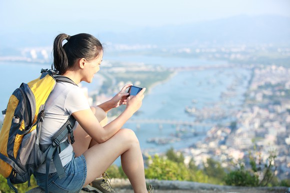 Woman using her smartphone, overlooking a bustling metropolis from an idyllic hilltop.