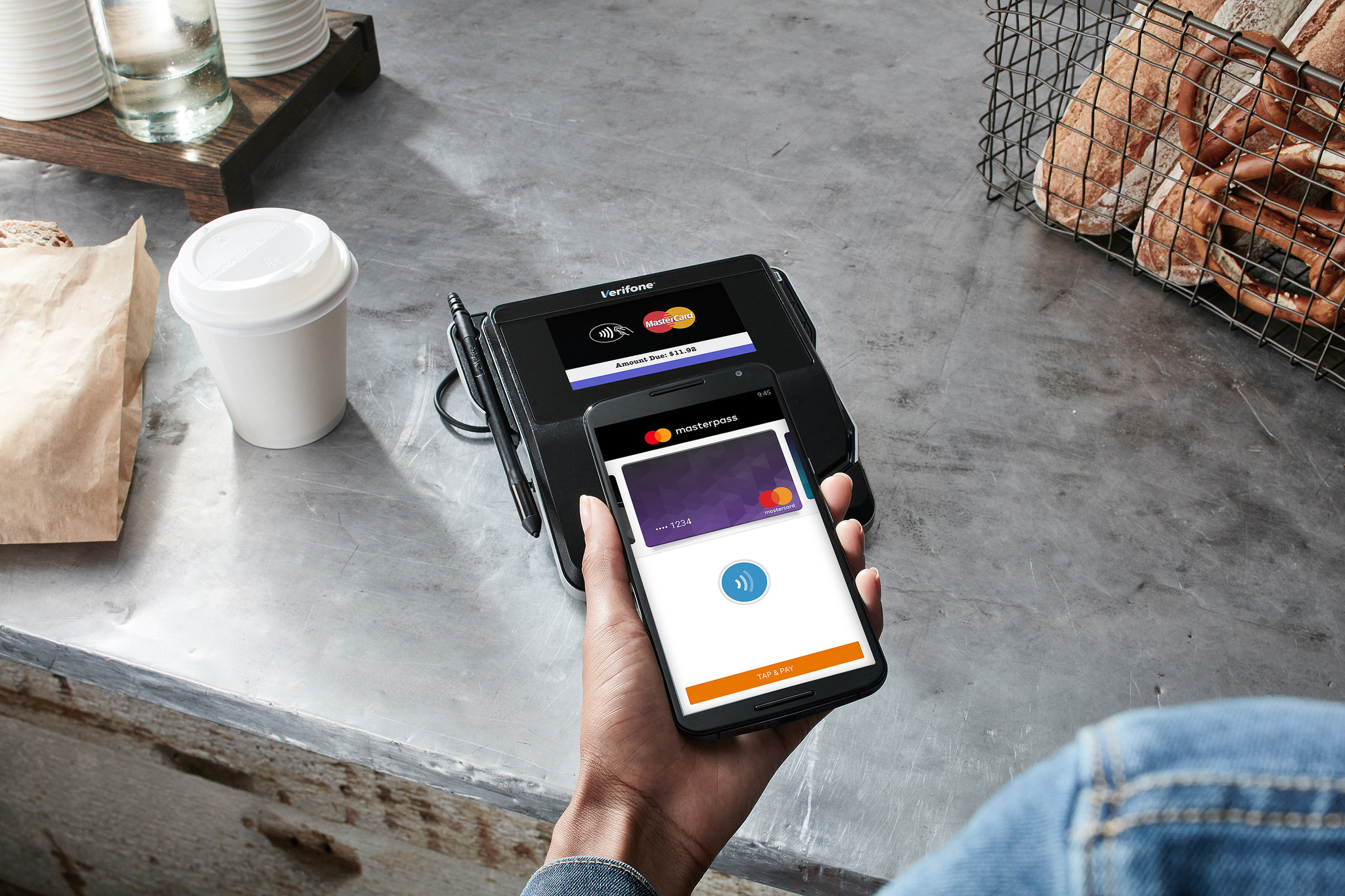 A hand holding a smartphone against a checkout counter at a restaurant with Mastercard payments app open on the screen.