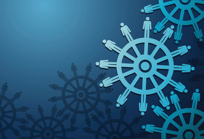 Vector image of wheels with cogs in the shape of business people on blue background