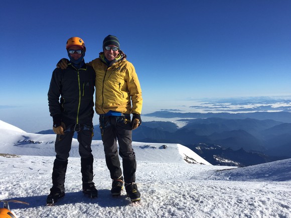 Two men in Eddie Bauer jackets stand on a mountaintop.