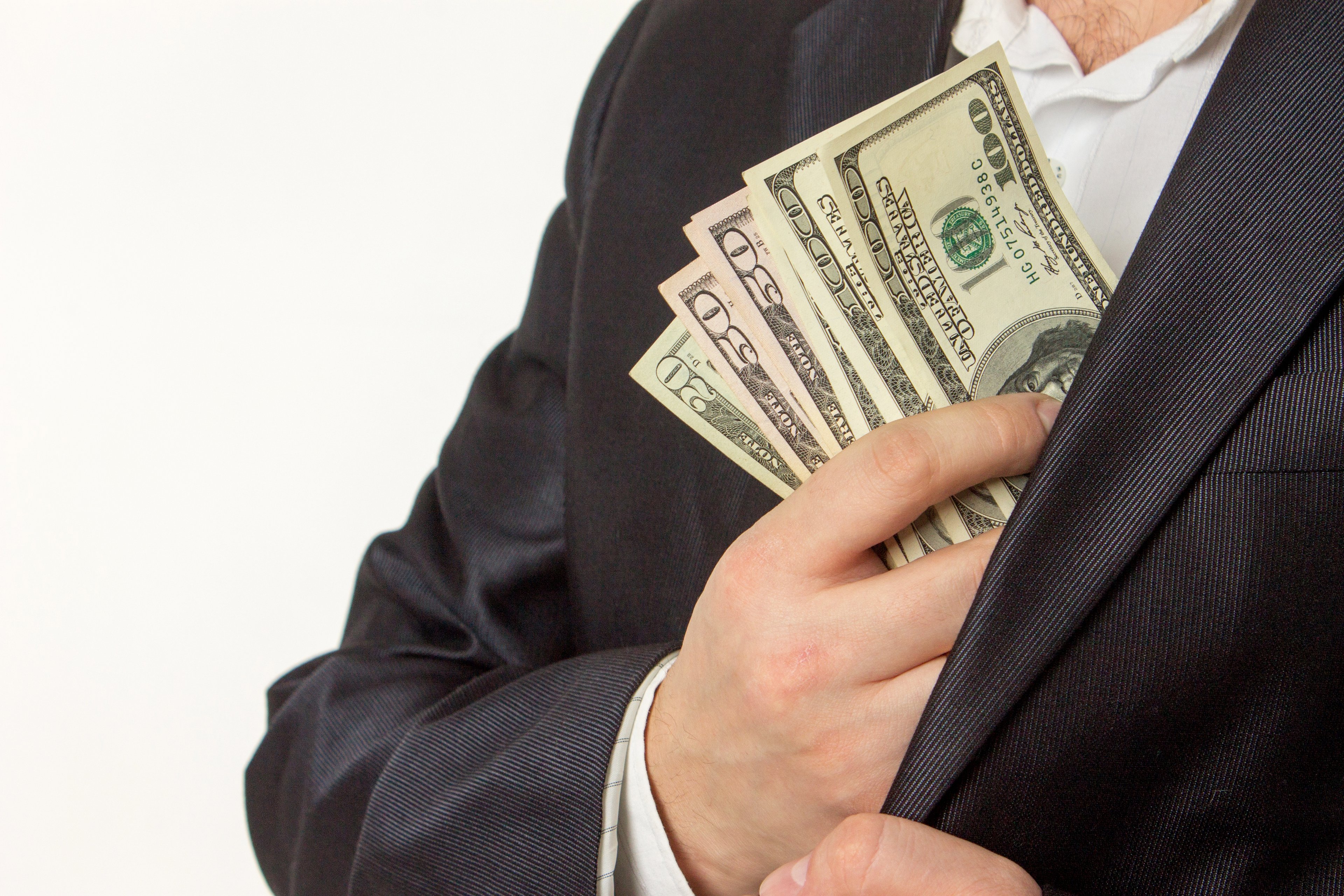 A businessman puts cash in an interior pocket of his suit jacket.