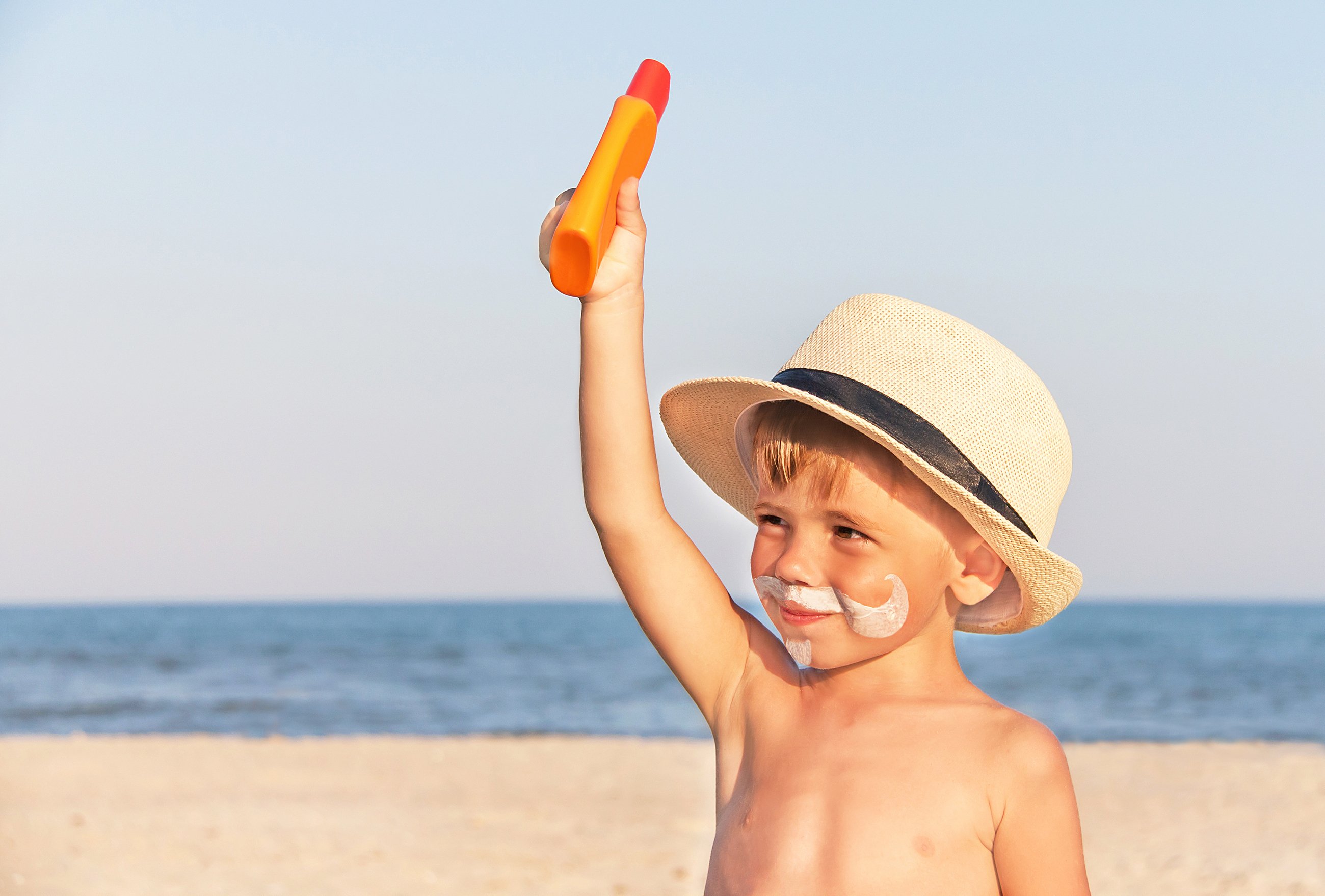 A young kid with a sunscreen beard on the beach.