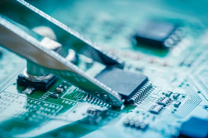 A set of tweezers touches a semiconductor on a device's logic board.