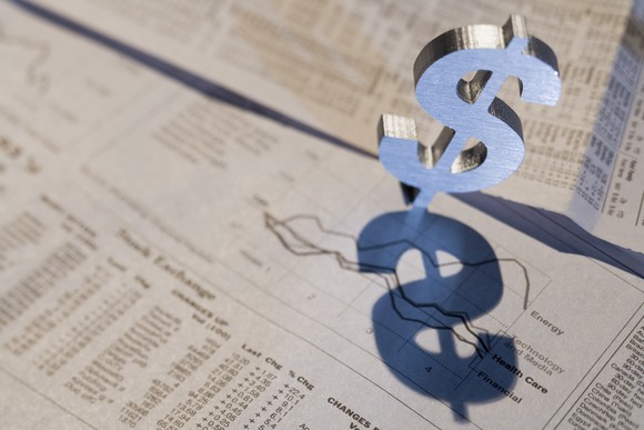 A dollar sign on top of a rising stock long-term stock chart in a newspaper. 