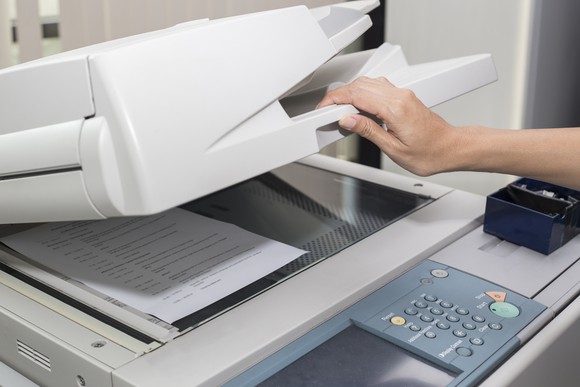 A hand lifting the cover of a photocopier.