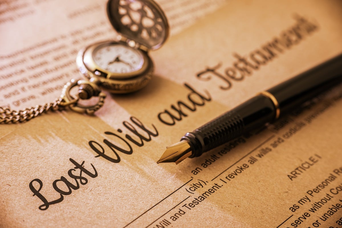 An ink pen rests on a will document, next to a pocket watch.