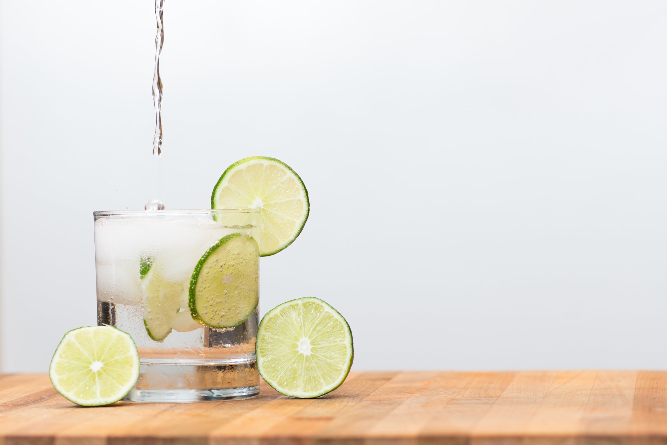 Sparkling water being pored into a glass with limes.